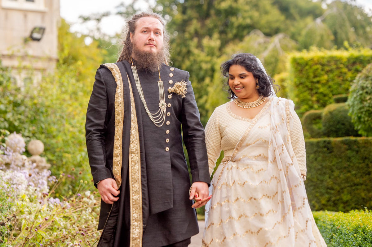 Sherni London bride and groom in fusion church wedding ceremony wearing white chikankari lucknowi lehenga and black asymmetric sherwani with gold buttons and trim
